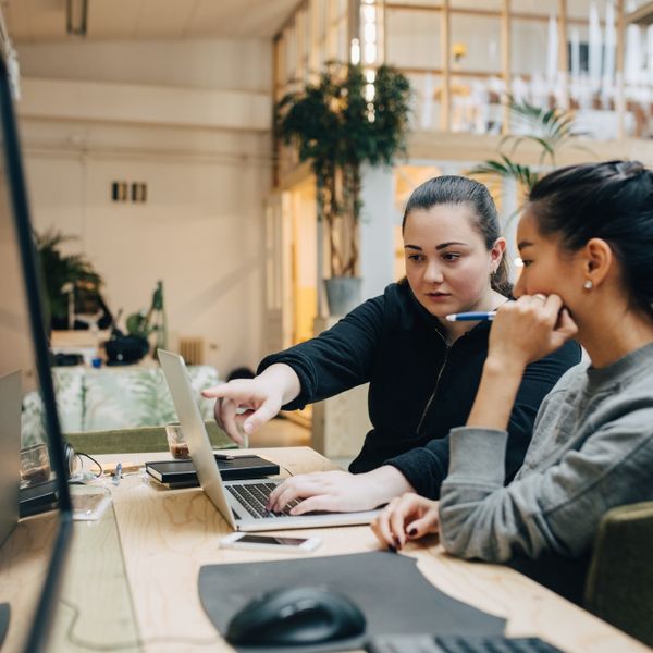 Two women discussing on laptop while sitting in office