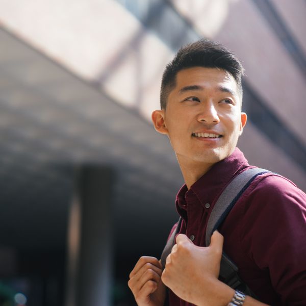 Asian man looking up and holding his backpack