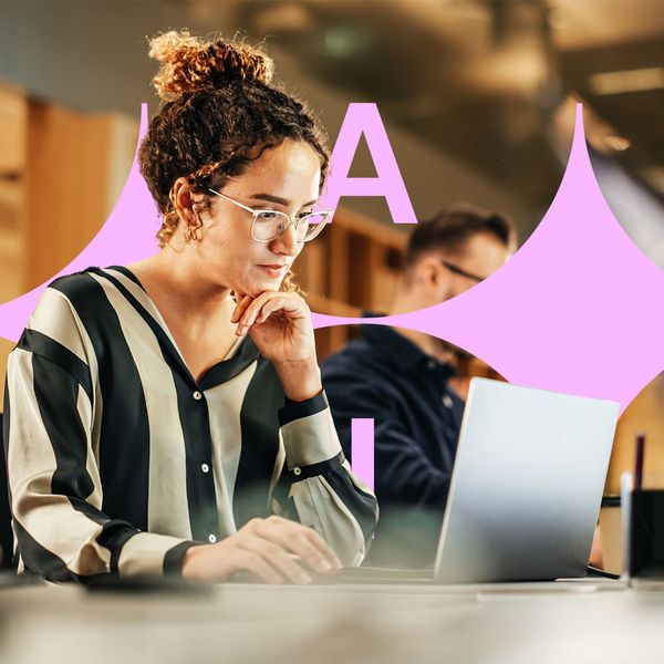 A woman wearing glasses and a striped shirt is working on a laptop in an office.
